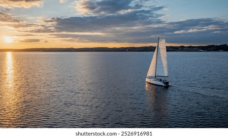 Sailboat gliding across calm waters at sunset. Sailboat at sunset with gentle waves and soft reflections on water. Concept of adventure and relaxation. Sailing on Flensburg Fjord with view of Denmark. - Powered by Shutterstock