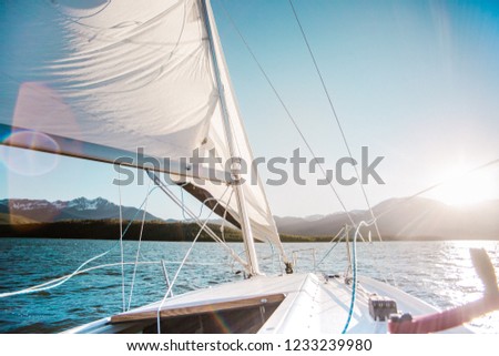 Sailboat in the mountain lake with the mountains on the background. White sail and sunset or sunrise. 