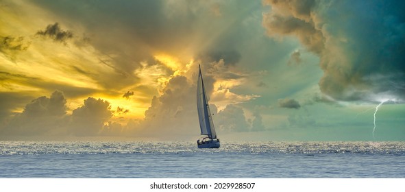 Sailboat navigating a silvery sea in a stormy cloudy sunset - Powered by Shutterstock