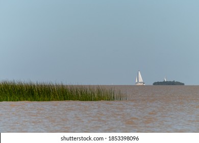 A Sailboat Near The Horizon Sailing At La Plata River In Front Of Colonia Del Sacramento