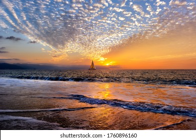 A Sailboat Is Sailing Along The Ocean At Sunset