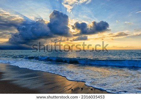A Sailboat Is Sailing Along The Ocean With A Wave Breaking On Shore And Sun Rays Breaking Through Clouds