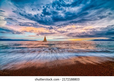 A Sailboat Sails Along The Ocean With A Colorful Cloudscape Overhead