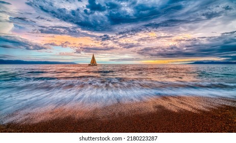 A Sailboat Sails Along The Ocean With A Colorful Cloudscape Overhead