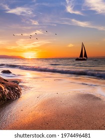 A Sailboat Sails Along The Ocean At Sunset In Vertical Image Format