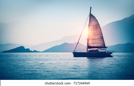 Парусная лодка в море в вечернем солнечном свете над красивыми большими горами фоне, роскошные летние приключения, активный отдых в Средиземном море, Турция