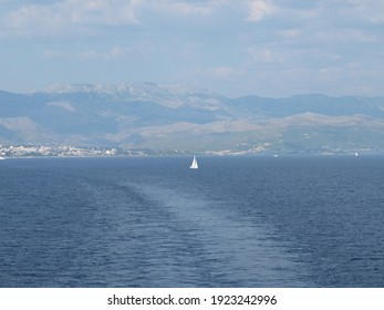 Sailboat In The Wake Of A Large Ship With Mountains In The Background