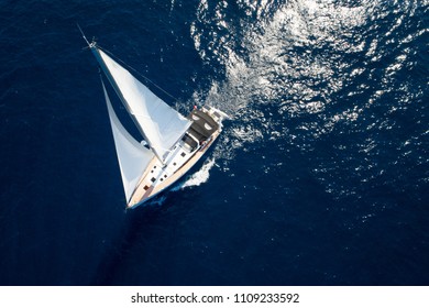 Sailboat while cruising / sailing at opened sea. Yacht with full sails up at the end of windy day. Sailing theme - aerial / drone background. Yachting background design.