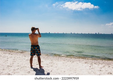 Sailboats sailing in the Black Sea at midday on the horizon. Taste of life. Competition of yachts on the wind. Various colors of ocean race. Spectator on sand beach of tropic island. Man shooting 