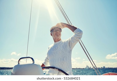 Sailing, Age, Tourism, Travel And People Concept - Happy Senior Man In Captain Hat On Steering Wheel And Looking Far Away Sail Boat Or Yacht Floating In Sea