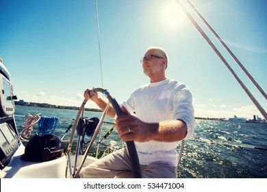 Sailing, Age, Tourism, Travel And People Concept - Happy Senior Man In Captain Hat On Steering Wheel And Navigating Sail Boat Or Yacht Floating In Sea