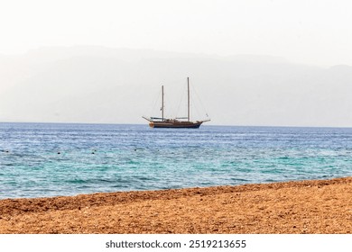 A sailing boat floats on a calm sea with a cargo ship in the distance. The misty horizon and gentle waves create a peaceful seascape scene - Powered by Shutterstock