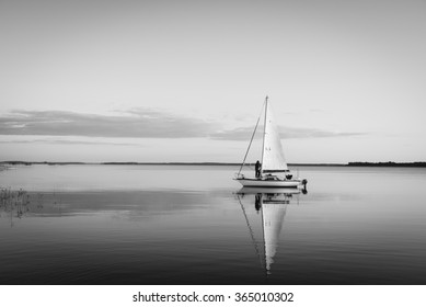 Sailing boat on a calm lake with reflection in the water. Serene scene landscape. Black and white horizontal photograph. - Powered by Shutterstock