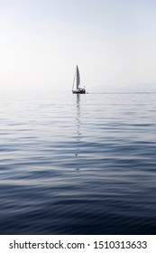 Sailing Boat On A Calm Sea Surface With Reflection In The Water