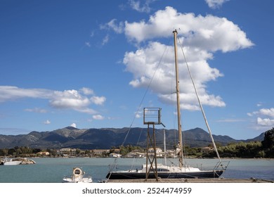 Sailing boat parked in a harbor. Town and mountains in the background. Blue sky with white clouds in the late summer. Astrakeri, Corfu, Greece. - Powered by Shutterstock