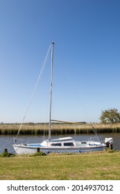 Sailing Boat. Small White Generic Yacht Moored On The Norfolk Broads UK. Inland River Vessel On Grass River Bank Mooring 