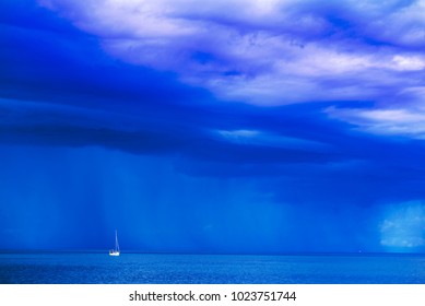 Sailing Boat At Stormy Sea Horizon With Dark Rainy Clouds In Background