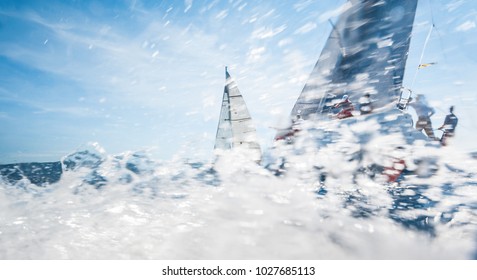 Sailing boats with spinnakers racing on open sea, water drift is motion blured