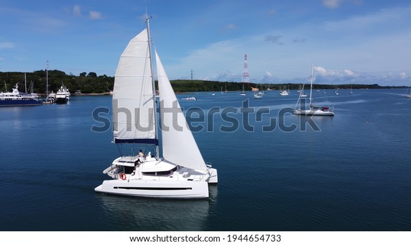 Sailing catamaran with open sails.\
Sailing\
catamaran in the middle of the sea in a tropical landscape. Sailing\
boat with open sails.\
Sailing catamaran on the background of a\
tropical coast with\
boats