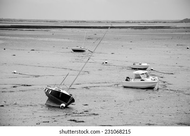 Sailing and fishing boats lying on the sea floor at low tide in small harbor near Saint-Malo in the dusk . Brittany, France. Business on the rocks / in low water metaphor. Aged photo. Black and white. - Powered by Shutterstock