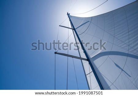Sailing with the wind at open sea ocean, summer holidays concept. Yacht wind filled sails on clear blue sky background. Looking up at the sky, sun shining, sunbeams on boat rigging, Low angle view