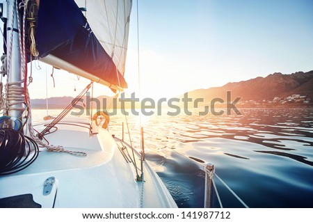 Sailing yacht boat on on ocean water at sunrise with flare and outdoor lifestyle