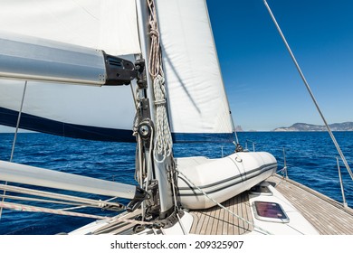 Sailing yacht going on her sails in calm weather with dinghy on board