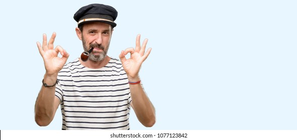 Sailor captain man smoking a tobacco pipe doing ok sign gesture with both hands expressing meditation and relaxation isolated over blue background