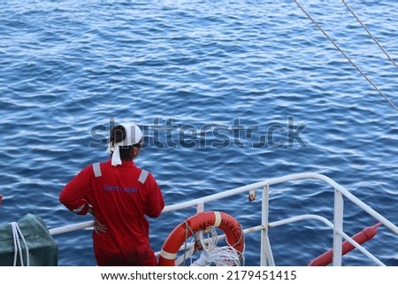 a sailor with a coverall and a headband is standing near the ship's railing and looking at the wide sea as if releasing heavy work. healing