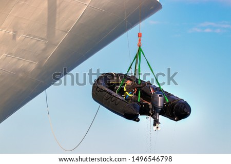 A sailor crew member is hanged with harness lowering a Rigid Hull Inflatable boat at sea.