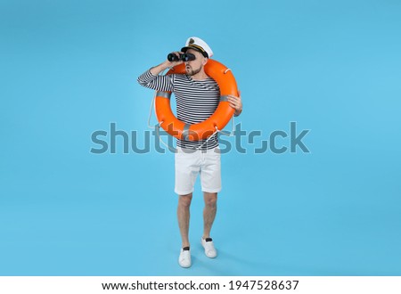 Sailor with orange ring buoy looking through binoculars on light blue background