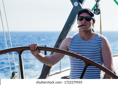 Sailor in a vest in the summer on a yacht in the ocean at the helm with a cigar in his mouth.