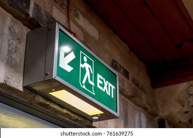 Saint Ives, Cambridgeshire, UK - Circa November 2017: Detailed View Of An Illuminated Emergency Exit Sign Seen Above An Interior Doorway, Located Within A Church, Required By Health And Safety.