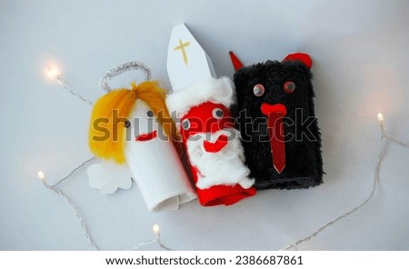 Saint Nicholas, Angel and Devil made by a child from toilet paper roll tubes on light blue background with Christmas lights. Simple diy creative Christmas idea. Eco-friendly recycle decoration.