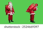 Saint nick in festive costume with gifts in famous red bag, spreading christmas spirit in studio. Santa claus embodiment with sack of presents looking around over full body greenscreen.