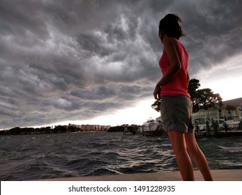 Saint Petersburg, FL, USA - 7/19/2019: A Young Woman Watches Dark Storm Clouds And Waves Build Over Tampa Bay, Florida. 