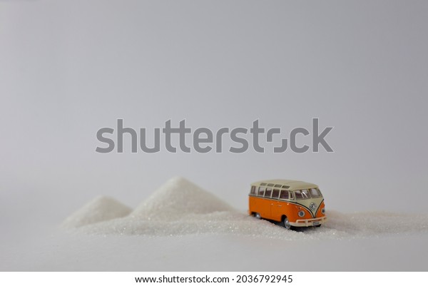Saint\
Petersburg, Russia - 08.08.2021 - Hippie bus toy in snow. Winter\
travel concept in miniature. Orange toy of Volkswagen transporter\
from 60s with sugar on table. Orange bull\
1960.