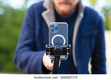 Saint Petersburg, Russia, 2021-09-06: Man Photographer, Videographer Taking Photo, Video On Blue Smartphone, IPhone 12 Phone With 3 Cameras On Selfie Stick With Stabilizer