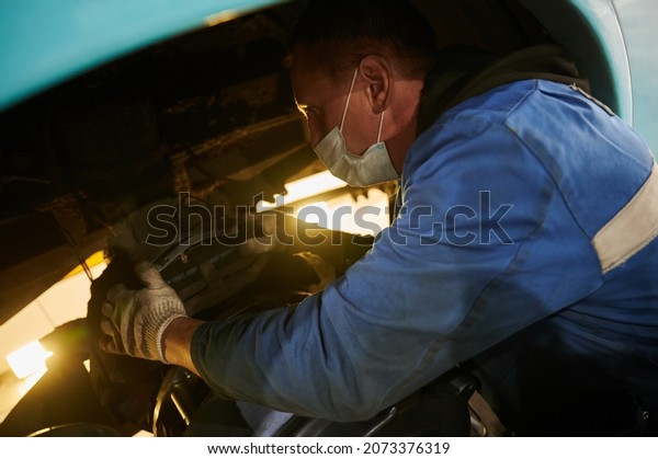 Saint Petersburg, Russia -\
September 30, 2021: An auto mechanic in a protective mask makes\
replacement of brake pads on a regular municipal bus in a\
workshop