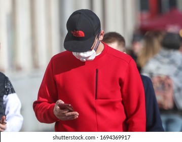Saint Petersburg, Russia-March 29, 2020: a Young man wearing a medical mask on his face to protect against the virus. A man in a red jacket black glasses and a cap is walking down the street