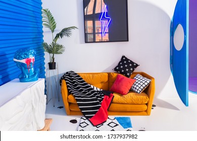 Saint Petersburg/Russia - March, 24 2020: Modern White-blue Room Interior In Color Block Style With Yellow Couch With Three Colorful Pillows And Striped Plush Plaid, A Tropical Plant And White Table.