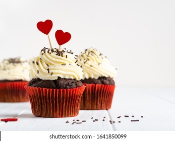 Saint Valentine's Day dessert, chocolate cupcakes with cream cheese frosting decorated with wooden hearts and chocolate sprinkles in red paper cups. White background, copy space, love concept. - Powered by Shutterstock