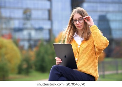 Saint-Petersburg, Russia - 03.03.2021: Happy Cheerful Positive Woman, Young Girl University Or College Student In Glasses Is Working On Her Tablet Computer IPad Pro Outdoors In Park, Campus