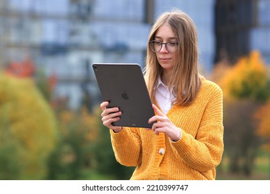 Saint-Petersburg, Russia - 03.03.2021: Happy Cheerful Positive Woman, Young Girl University Or College Student In Glasses Is Working On Her Tablet Computer IPad Pro Outdoors In Park, Campus