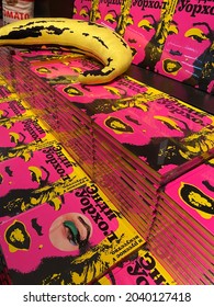 Saint-Petersburg, Russia - 12 Of September 2021. Shelves With ‘Andy Warhol’ Books In Pink And Yellow Colors And A Yellow Banana Toy On The Shelves In The Store At The Exhibition. Editorial Use Only.