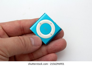 Saint-Petersburg, Russia - May 10, 2022: Blue iPod Shuffle in a man's hand. A small square music player with a big white button on the table.
