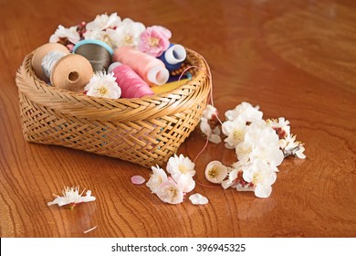 Sakura in wicker basket with spools of thread on wooden background