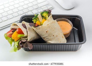 Salad box for take away (Pita bread wrapped with mixed vegetables) with thousand island dressing in plastic box have keyboard and mouse as blur background on white isolated, in rush hours.