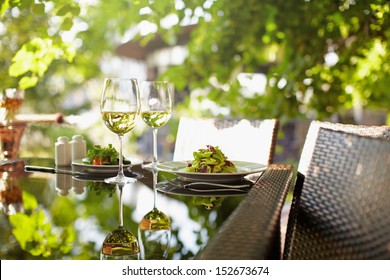 A salad and a couple wineglasses on a table outdoor with hookah on the background - Powered by Shutterstock