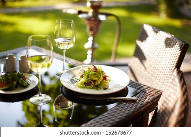 A salad and a couple wineglasses on a table outdoor with hookah on the background - Powered by Shutterstock